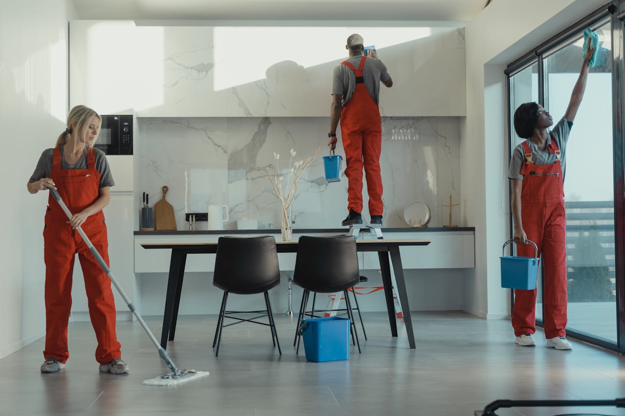 expertise-01 Group of cleaners in red uniforms mopping and wiping glass in a modern dining room.